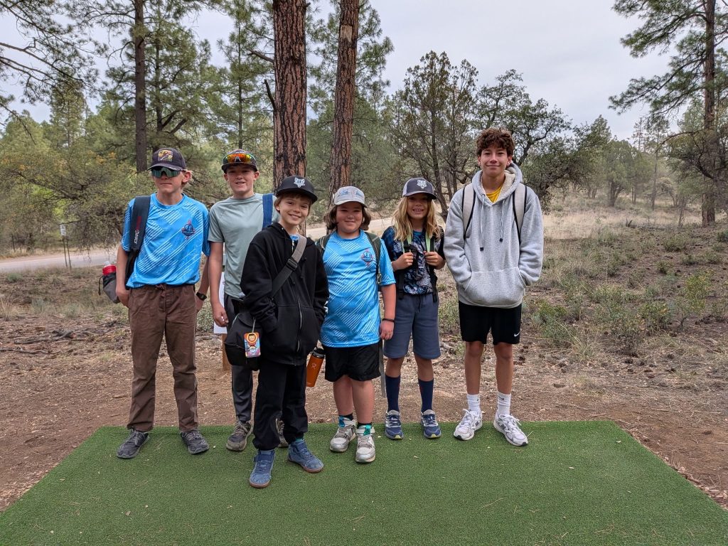 Six players posing together on a tee pad among pine trees at the 2026 Kneeling Nun Classic.